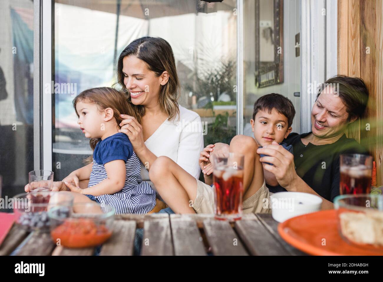 Parents heureux assis avec des enfants à la table contre la porte vitrée Banque D'Images