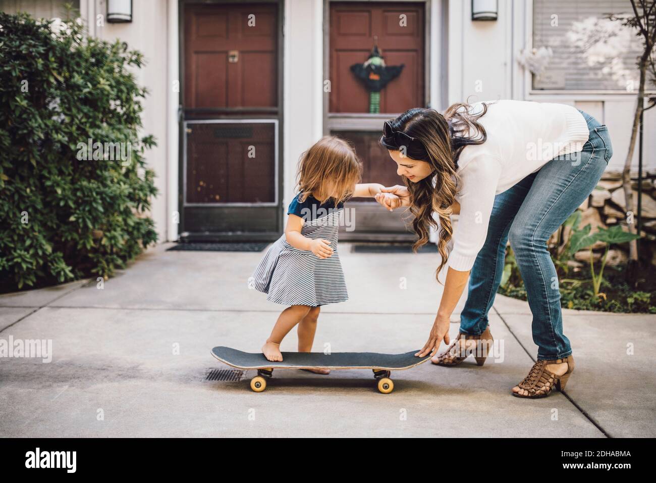 Elle fait du skateboard avec l'aide d'une mère souriante sur une piste de marche Banque D'Images