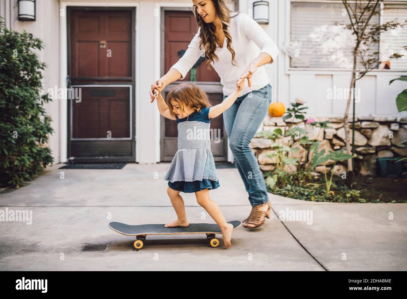 Fille souriante se balançant sur le skateboard avec l'aide de la mère chemin de pied Banque D'Images