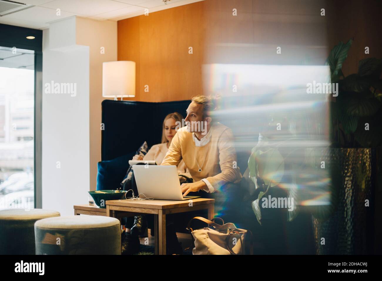 Homme d'affaires regardant loin en étant assis avec un ordinateur portable par un collègue cafétéria de bureau vue du verre Banque D'Images