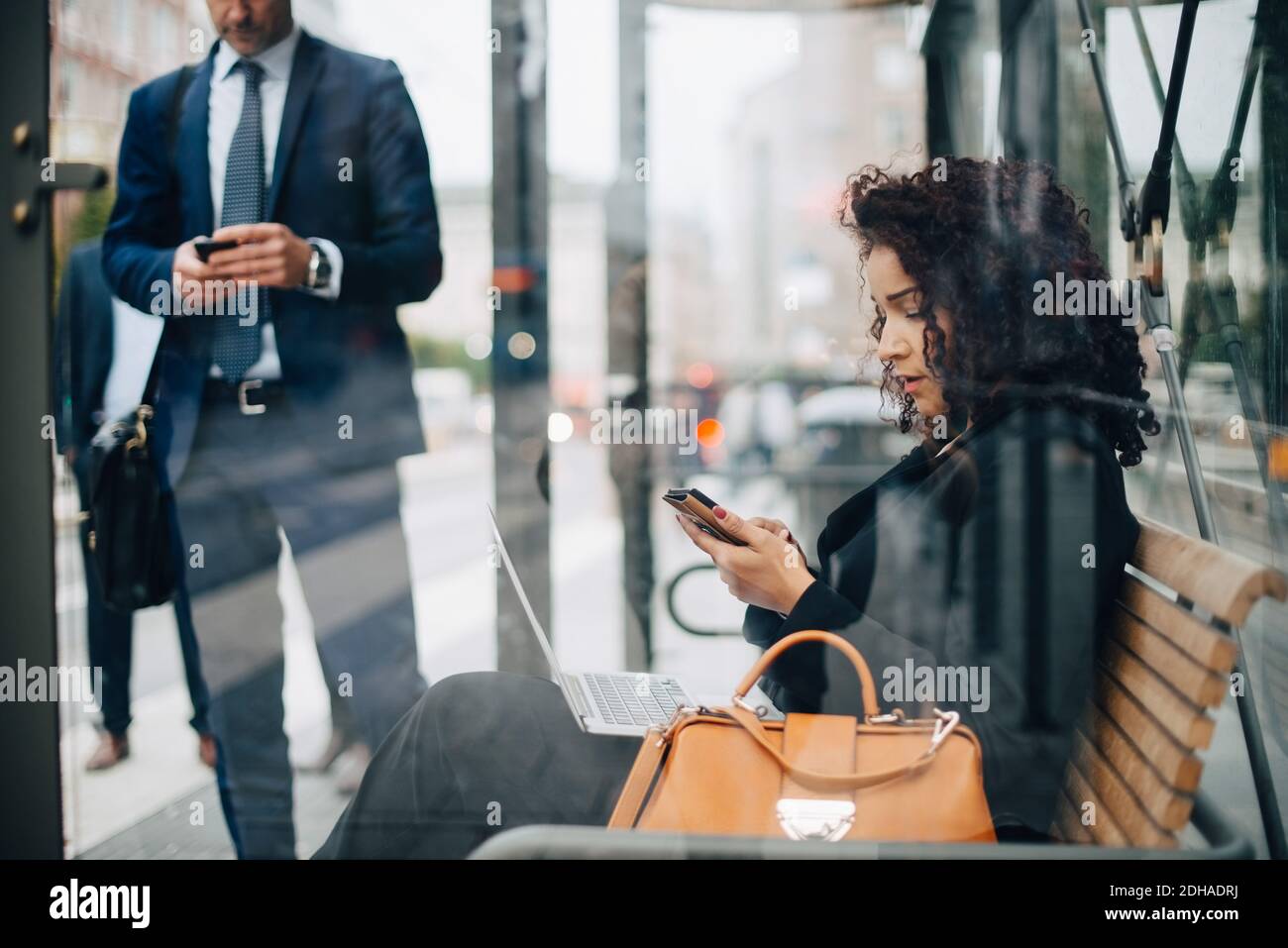 Les gens d'affaires qui utilisent des téléphones intelligents en attendant dans un abri de bus vue depuis le verre Banque D'Images