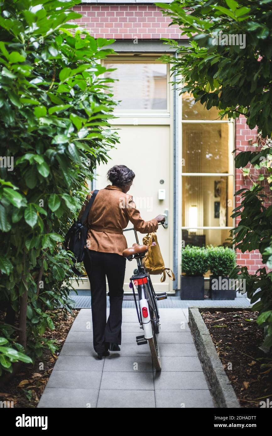 Vue arrière d'une femme architecte avec vélo debout contre la maison Banque D'Images