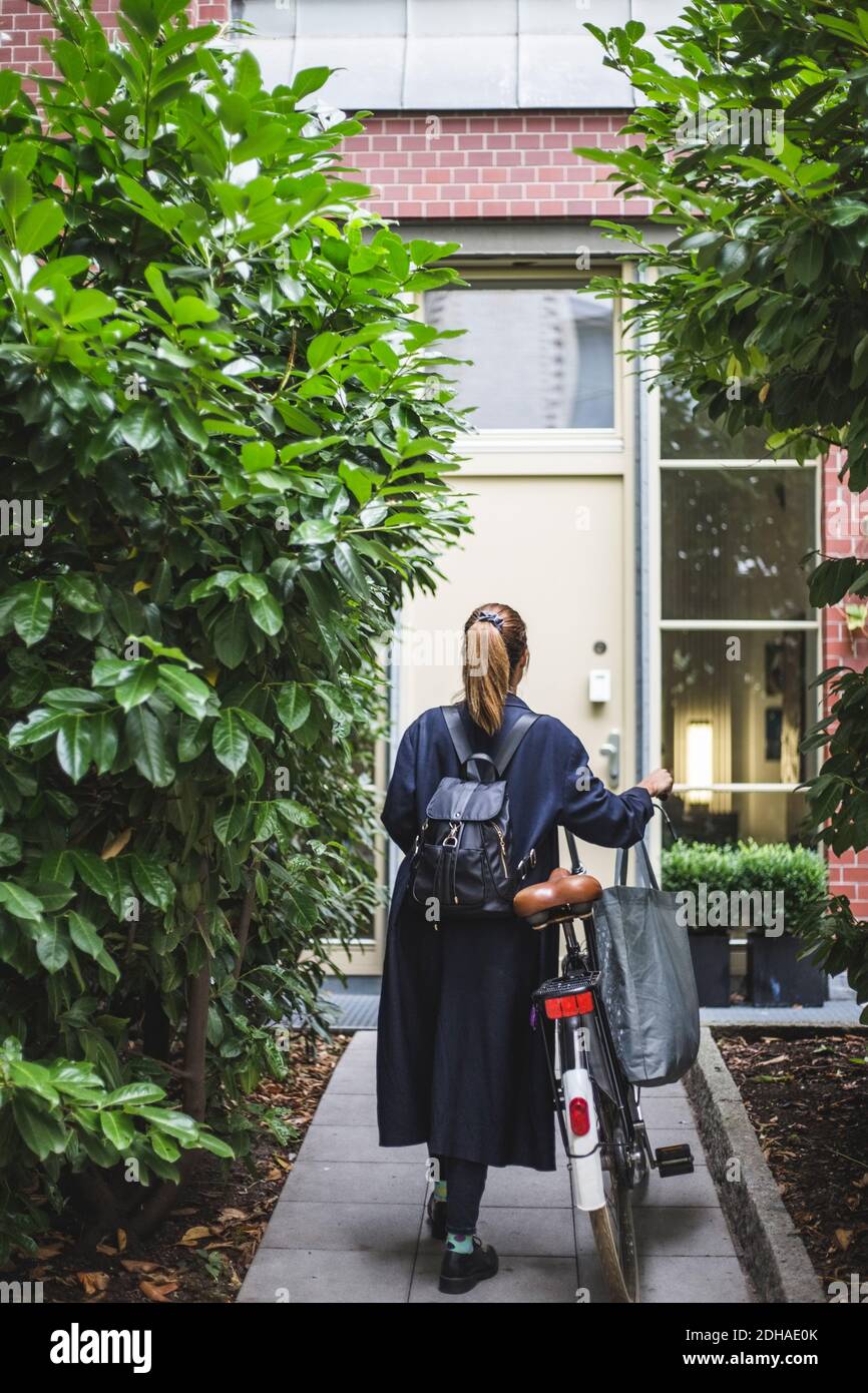 Vue arrière d'une femme architecte avec marche à vélo contre la maison Banque D'Images