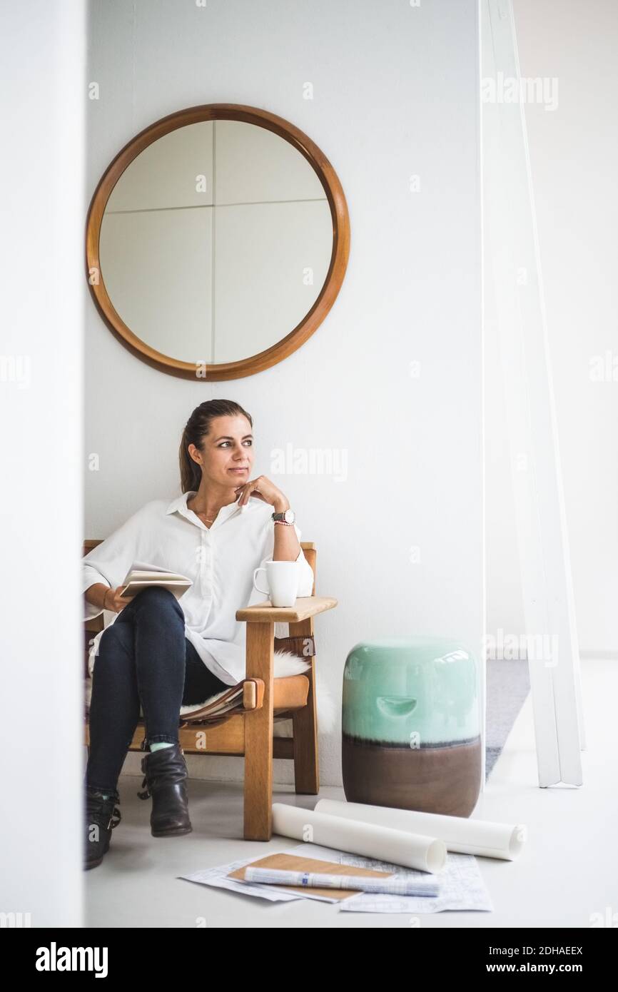 Femme design professionnel regardant loin en étant assis sur une chaise à bureau à domicile Banque D'Images