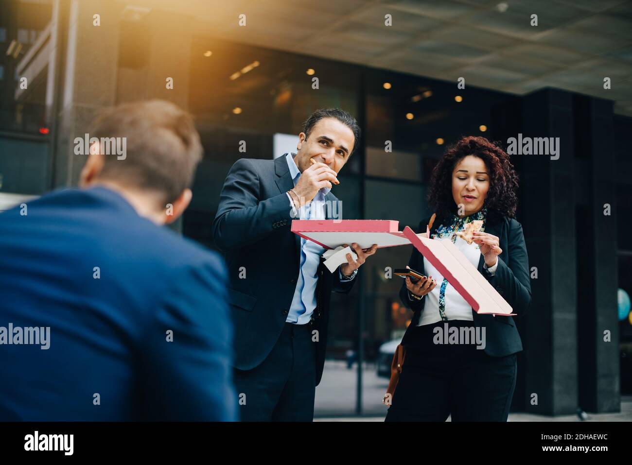 Vue à angle bas de l'homme d'affaires et de la femme d'affaires qui mangent de la pizza contre bâtiment pendant le déjeuner Banque D'Images