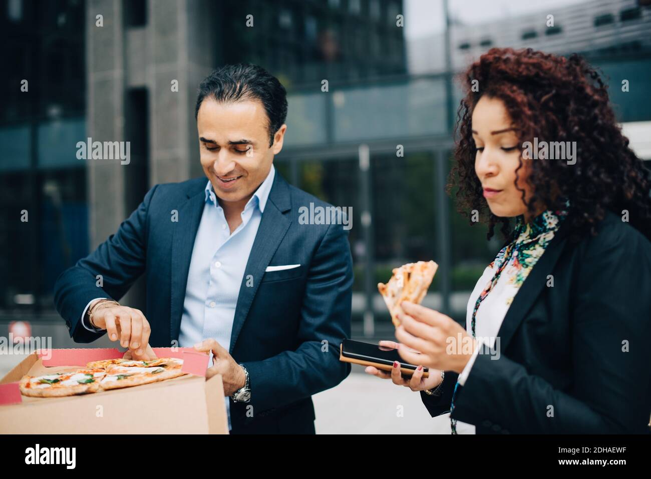 Homme d'affaires et femme d'affaires mangeant de la pizza contre la construction pendant le déjeuner Banque D'Images