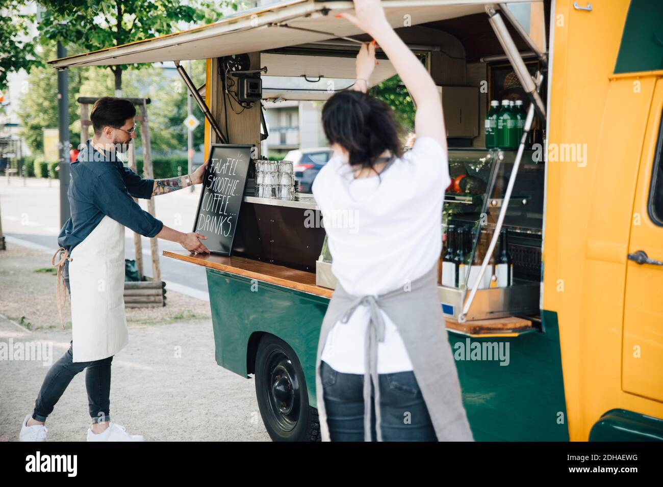 Le propriétaire masculin ajuste la carte sur le stand de concession tandis que la collègue de travail féminine ouverture de l'abat-jour du chariot élévateur Banque D'Images