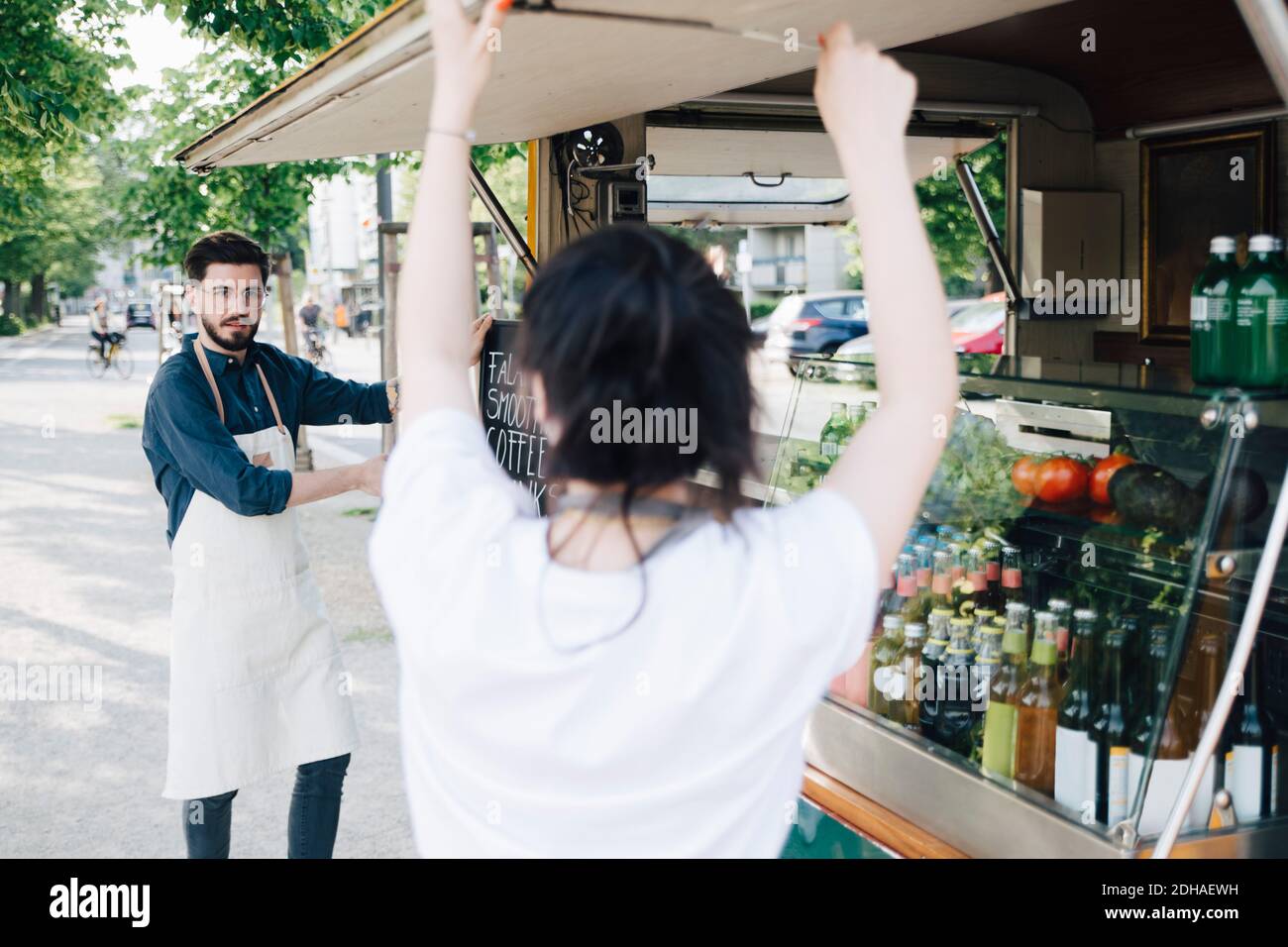 Le propriétaire mâle avec un tableau regardant la femme collègue ouvrant l'ombre de camion alimentaire Banque D'Images