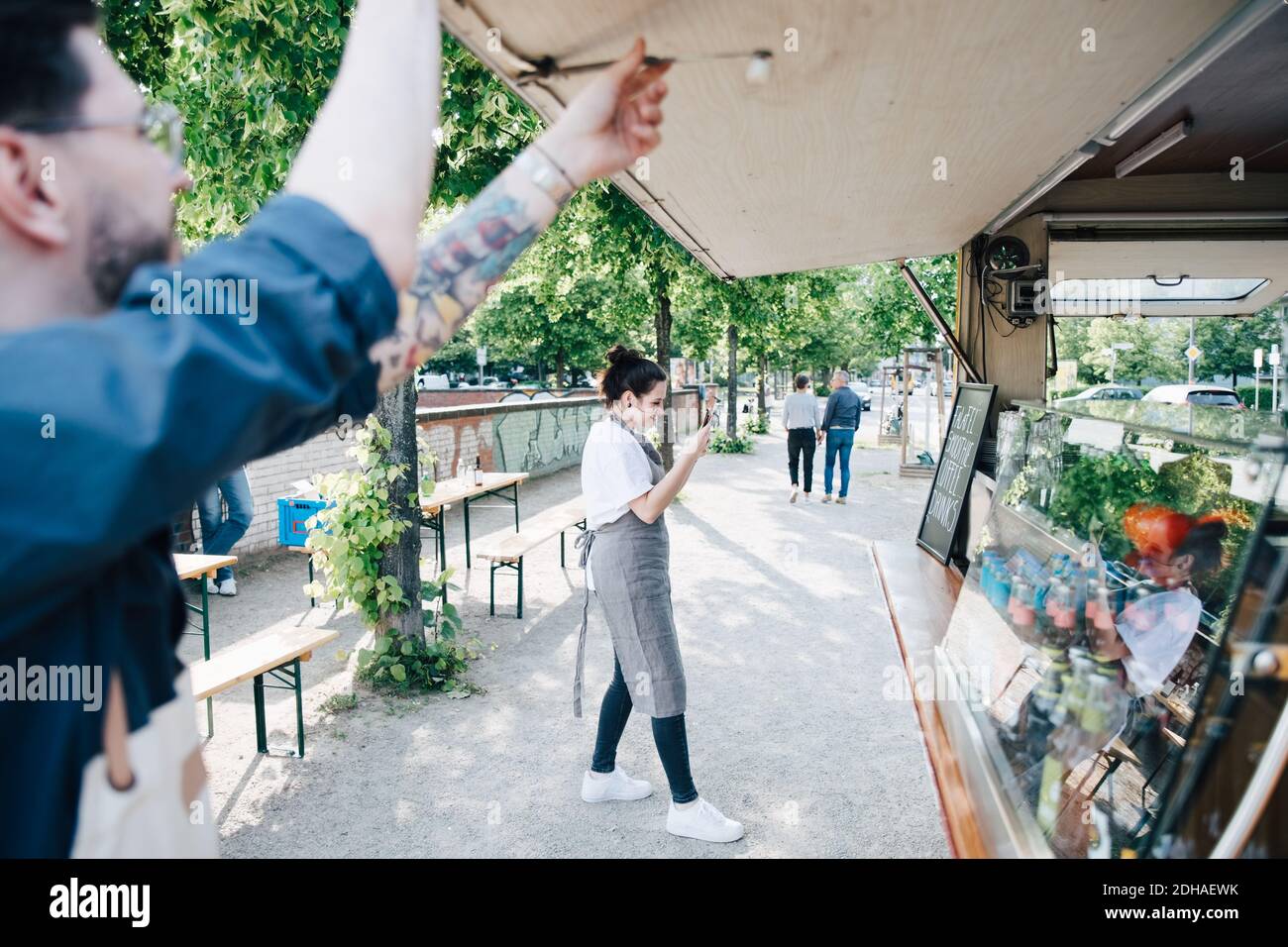 Femme propriétaire photographiant la carte à l'aide d'un smartphone pendant qu'un collègue est un homme ouverture de l'abat-jour du chariot élévateur Banque D'Images