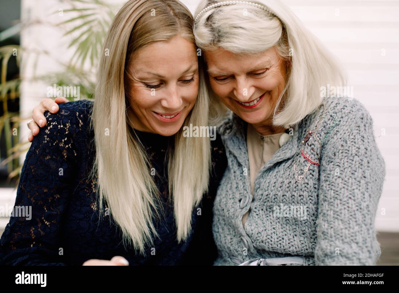 Mère et fille souriantes avec le bras assis contre le mur Banque D'Images