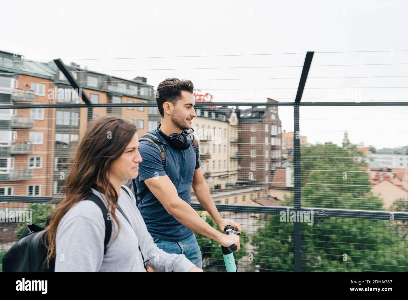 Amis hommes et femmes utilisant des scooters de poussée sur le pont ville contre ciel Banque D'Images