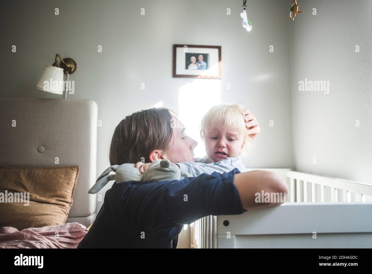 Père consolant bébé blond pleurs dans un berceau avec tendre l'amour à la maison Banque D'Images