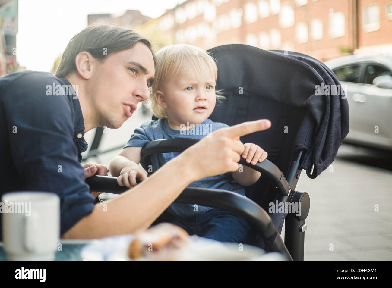 Un père qui se fait remarquer en regardant loin avec son fils au café-terrasse en ville Banque D'Images