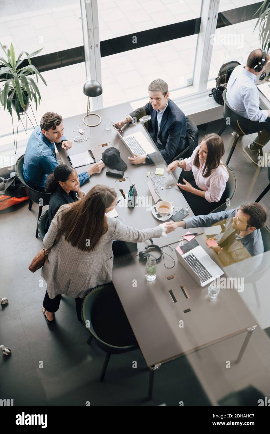 Vue en grand angle de l'équipe qui regarde les professionnels qui se secouent la main dans un espace de travail créatif Banque D'Images