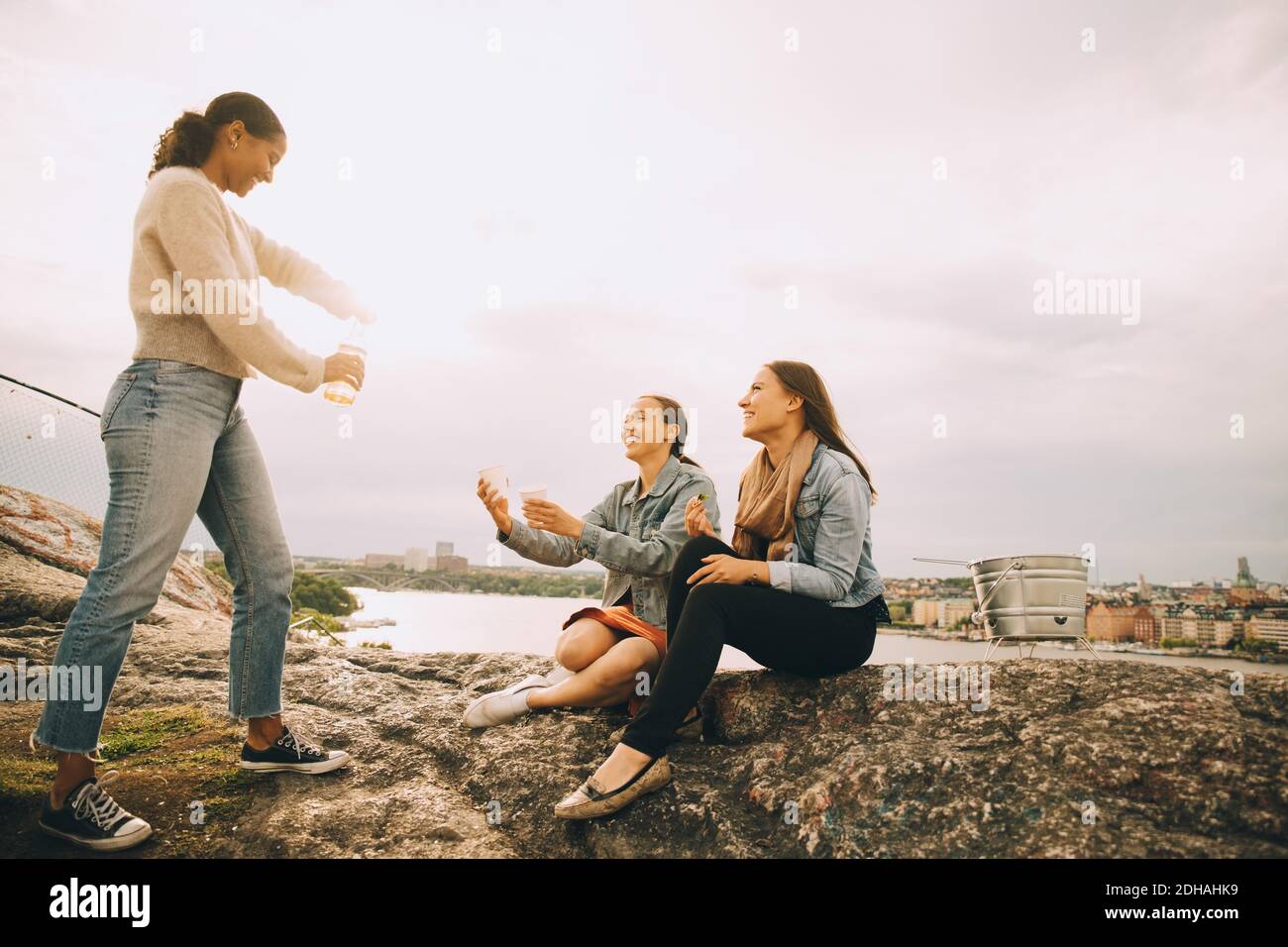 Femme donnant une boisson à des amis sur la formation de roche au bord du lac contre le ciel Banque D'Images
