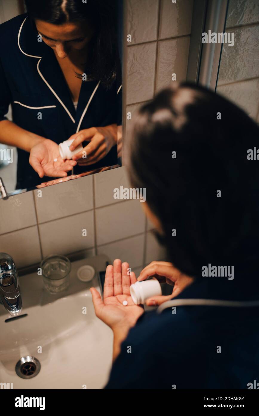 Femme réfléchissant dans le miroir tout en prenant des médicaments par le lavabo à salle de bains Banque D'Images