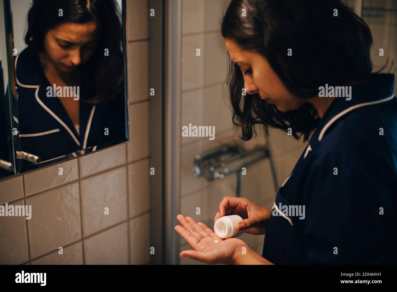 Femme prenant des pilules tout en se tenant devant le miroir à salle de bains Banque D'Images
