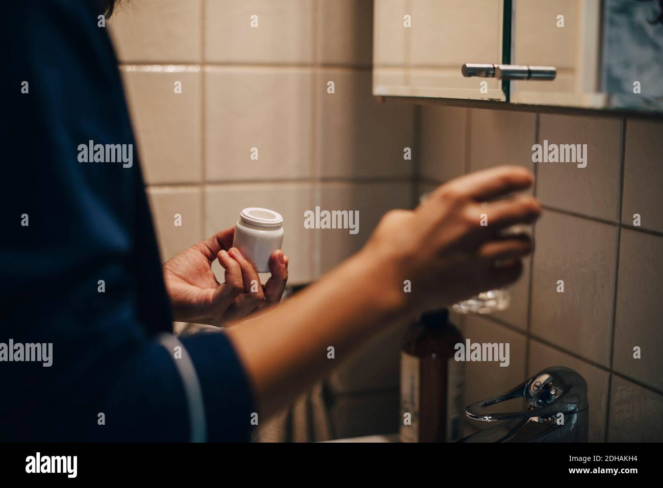 Image rognée d'une femme tenant du verre et des pilules debout dans la salle de bains Banque D'Images