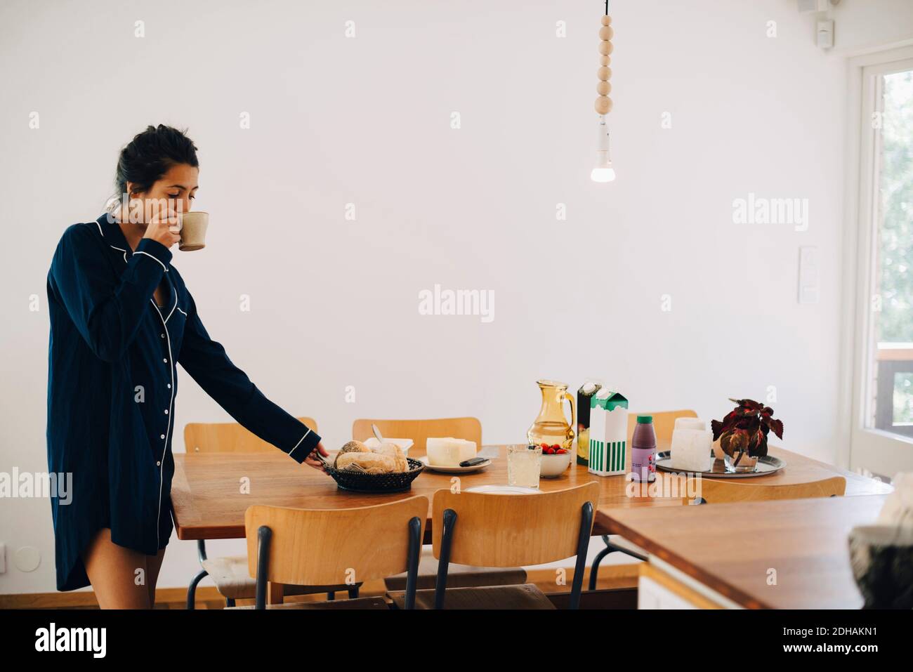 Femme buvant du café tout en regardant le petit déjeuner à table mur Banque D'Images