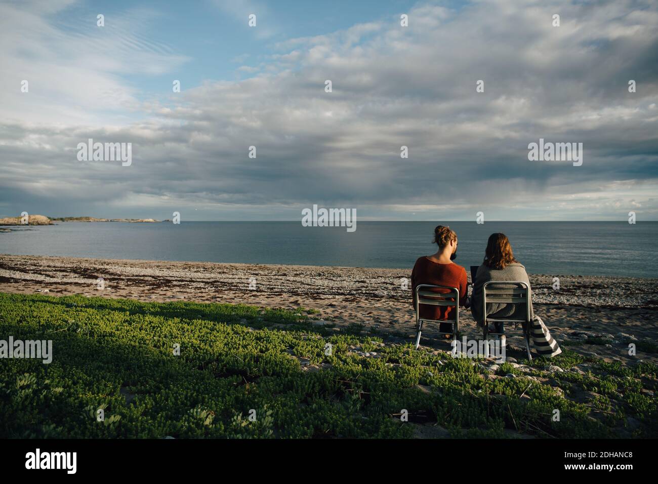 Vue arrière des amis assis sur des chaises au bord de la mer contre le ciel nuageux Banque D'Images