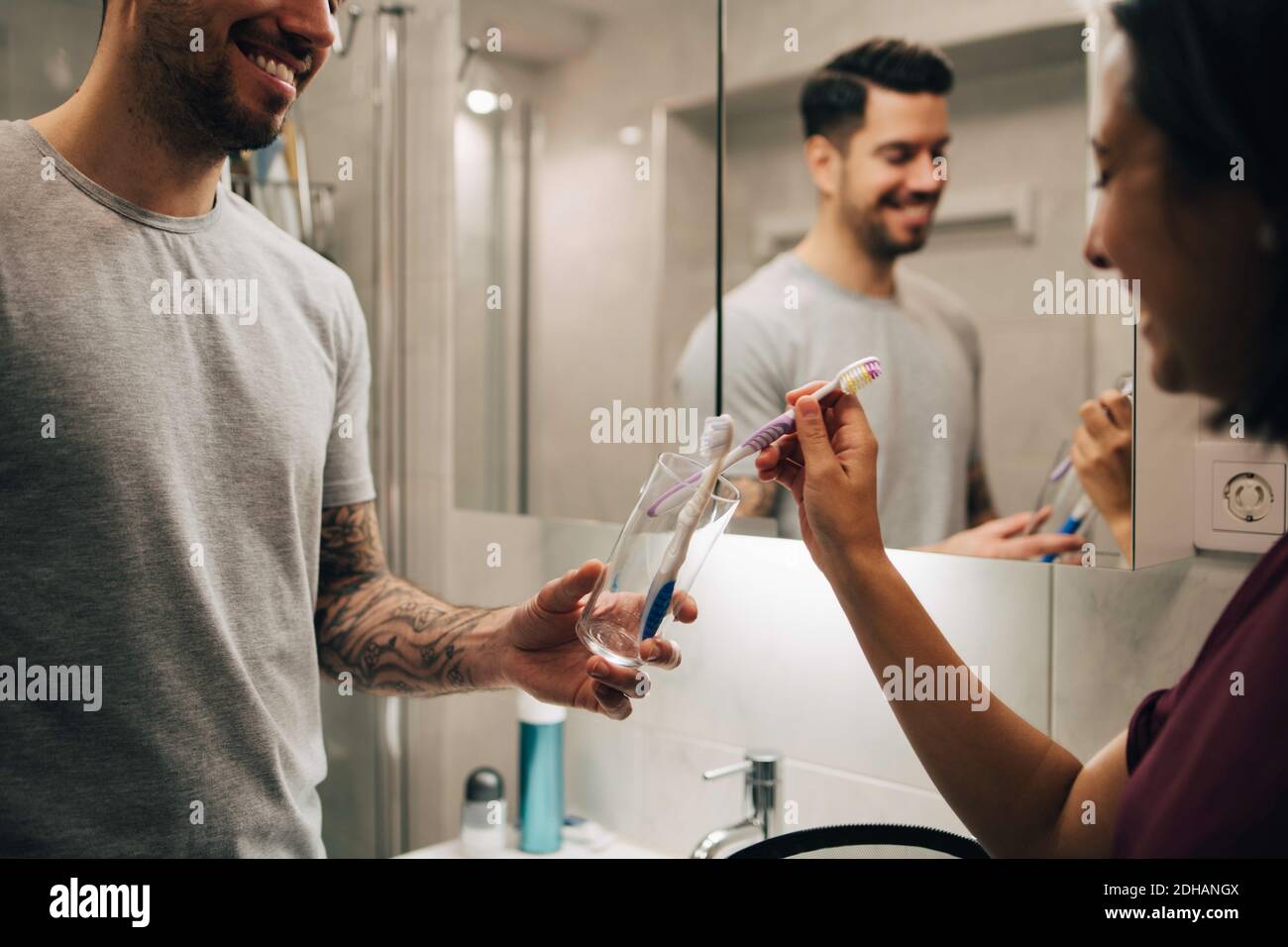 Couple souriant organisant des brosses à dents dans un contenant à côté d'un miroir dans la salle de bains Banque D'Images