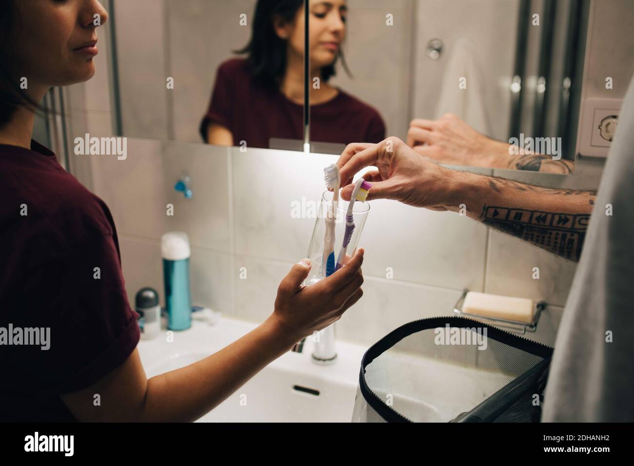 Homme et femme tenant les brosses à dents dans un récipient à l'évier éclairé Banque D'Images