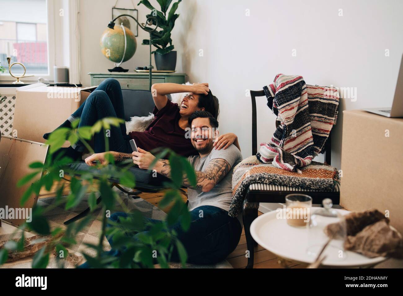 Couple heureux utilisant un smartphone tout en se reposant à la maison pendant l'emplacement Banque D'Images