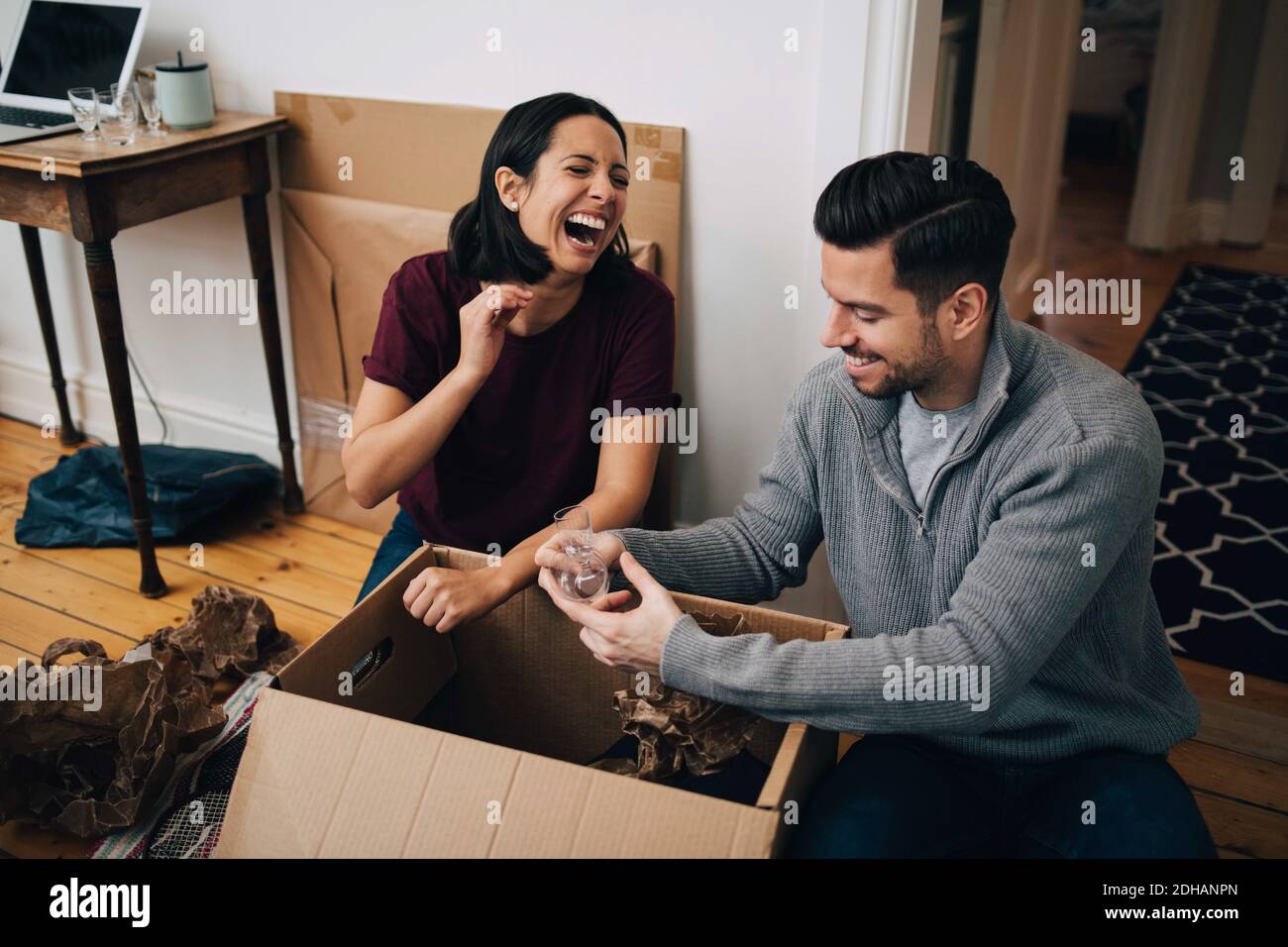 Couple riant déballer la boîte en carton tout en étant assis sur le sol à accueil Banque D'Images