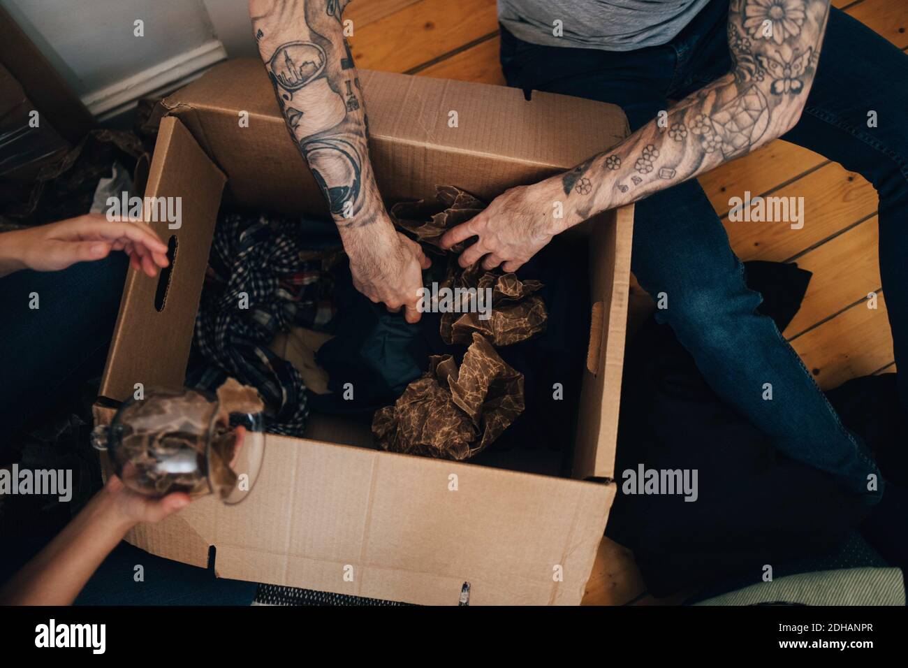 Image rognée d'un couple qui déballe la boîte en carton tout en étant assis sol à la maison Banque D'Images