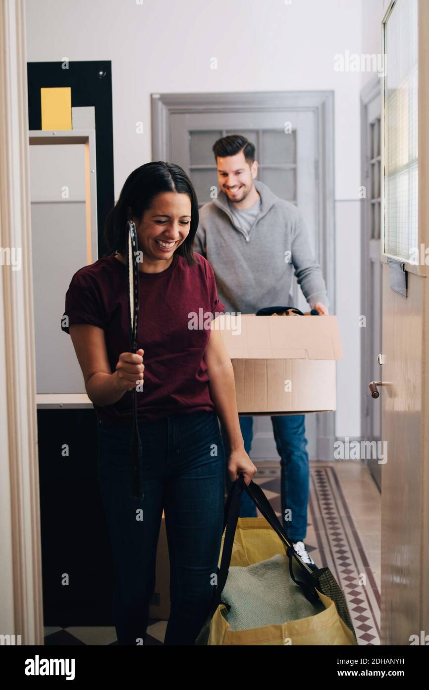Un couple souriant porte sa boîte et son sac tout en marchant dans le couloir à la maison Banque D'Images