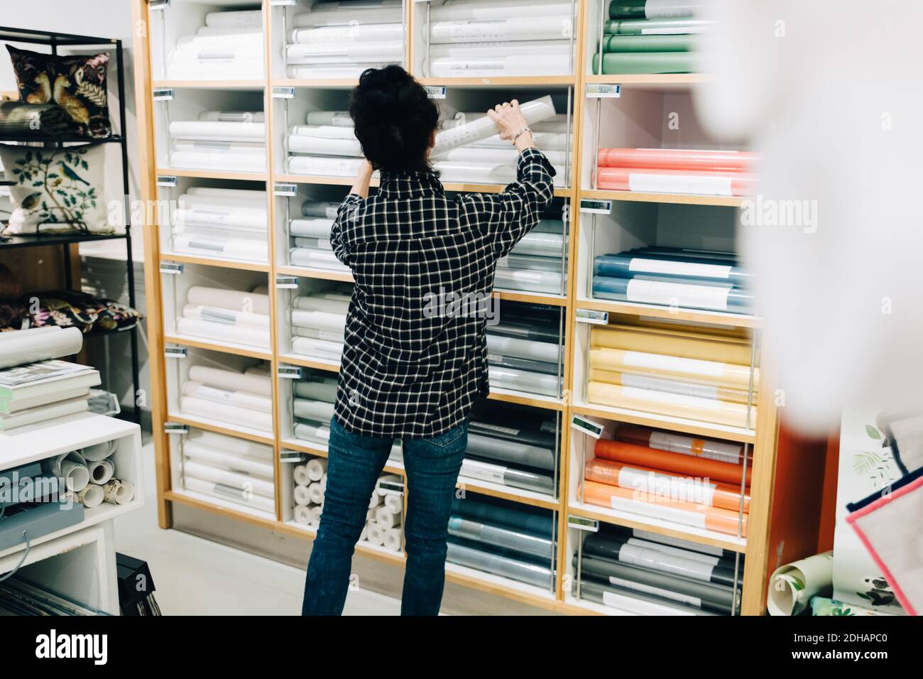 Vue arrière de la vendeuse senior qui organise les fonds d'écran dans le rack Banque D'Images