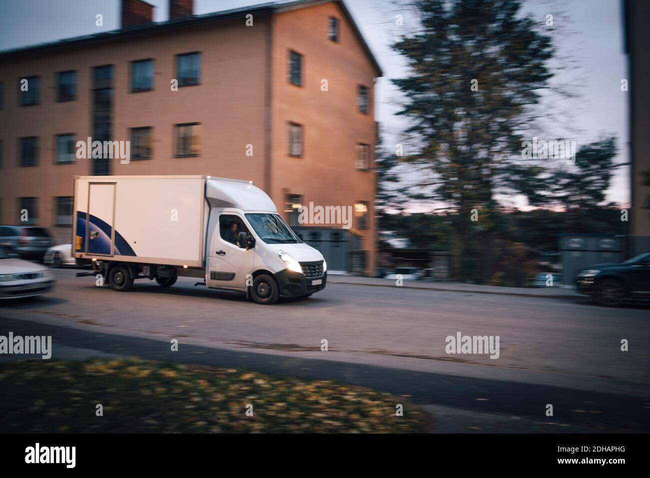 Le camion de livraison se déplace sur la route en construisant dans la ville contre ciel au coucher du soleil Banque D'Images