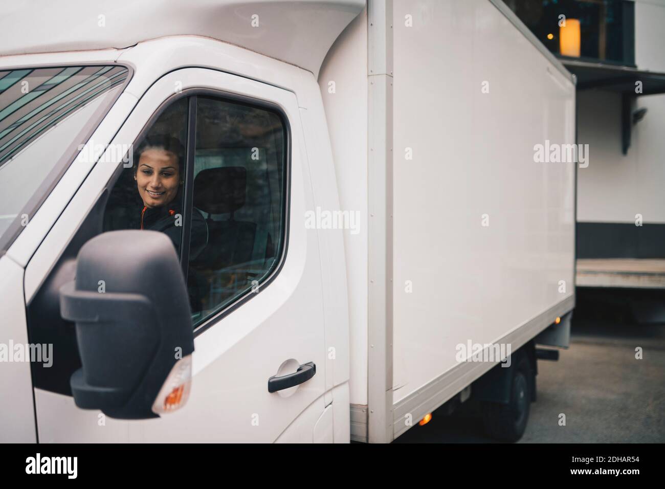 Femme souriante conduisant une camionnette de livraison blanche en ville Banque D'Images
