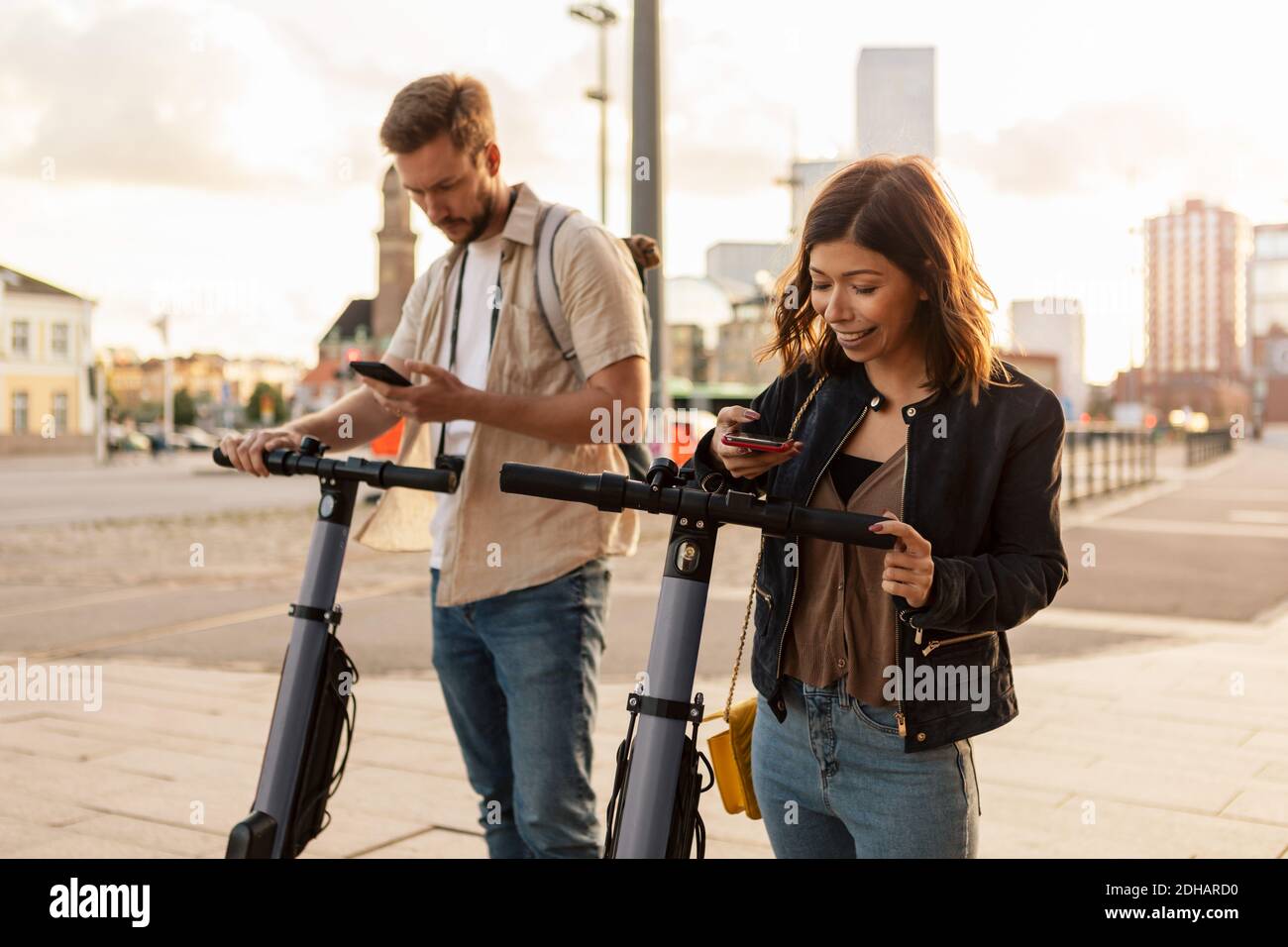 Les navetteurs hommes et femmes numérisent via un téléphone mobile tout en déverrouillant scooters électriques en ville Banque D'Images