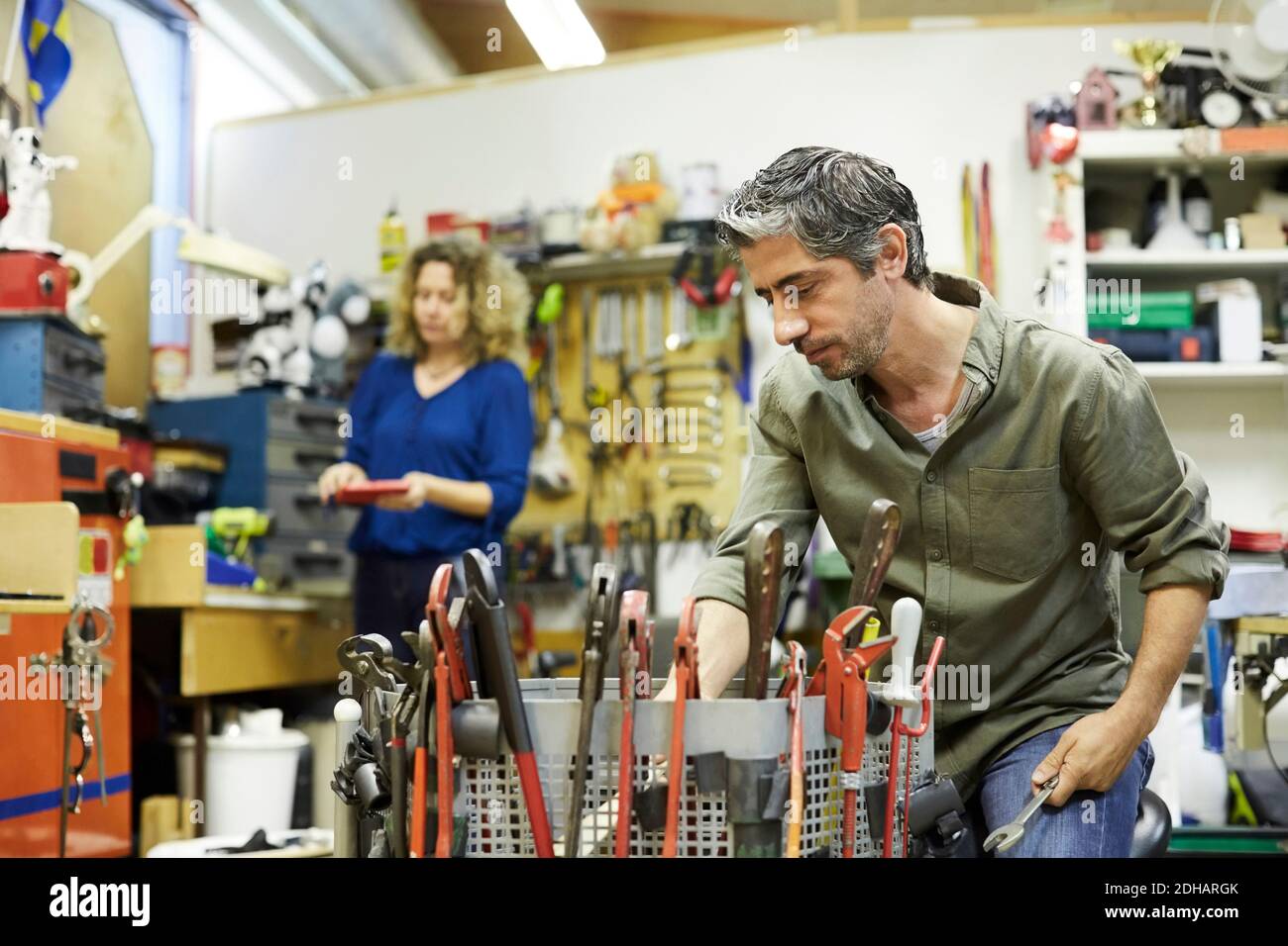 Un homme mature travaillant avec des outils contre une collègue féminine chez atelier Banque D'Images