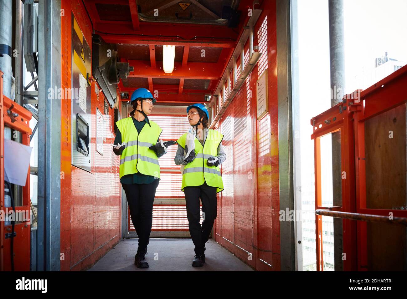 Toute la longueur de femmes ingénieurs discutant en marchant dans le fret ascenseur sur le chantier Banque D'Images