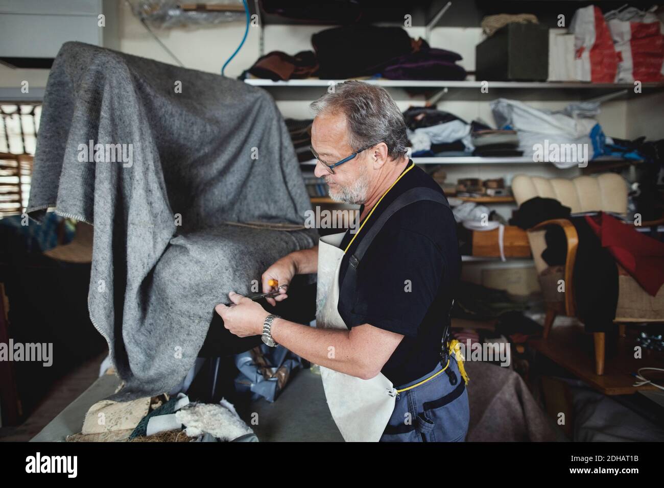 Un homme de premier plan coupe du tissu gris en se tenant à l'atelier Banque D'Images