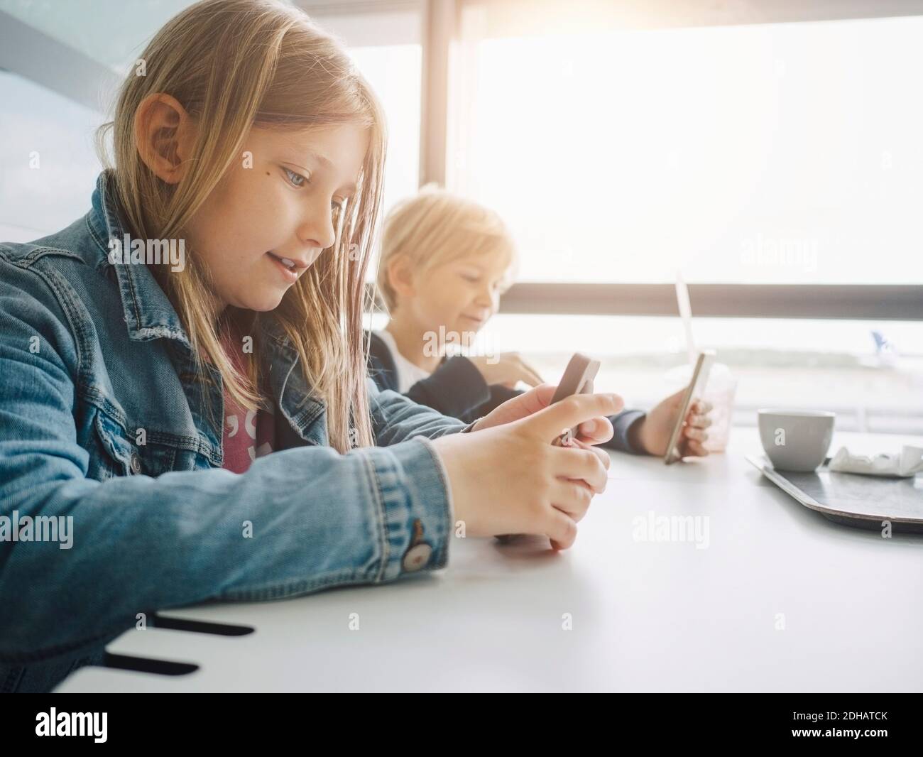 Frères et sœurs utilisant des smartphones assis à une table Banque D'Images