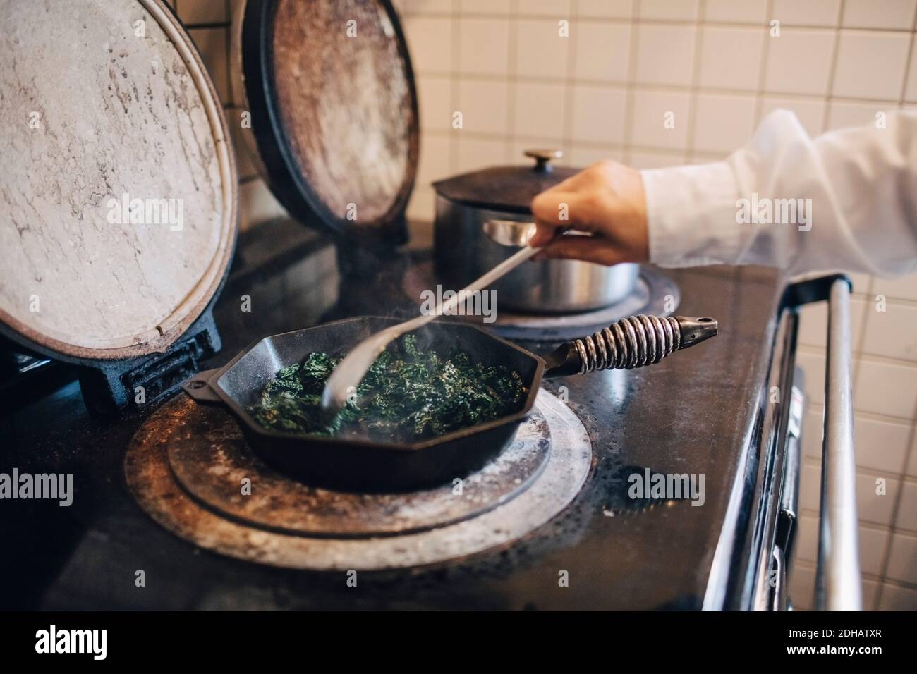 Main de chef cuisiné en remuant le chou kale dans une casserole cuisinière dans la cuisine du restaurant Banque D'Images