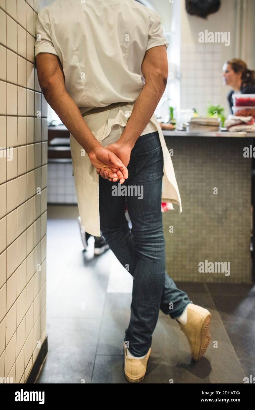 Section basse de chef masculin debout avec les mains derrière le dos dans la cuisine du restaurant Banque D'Images