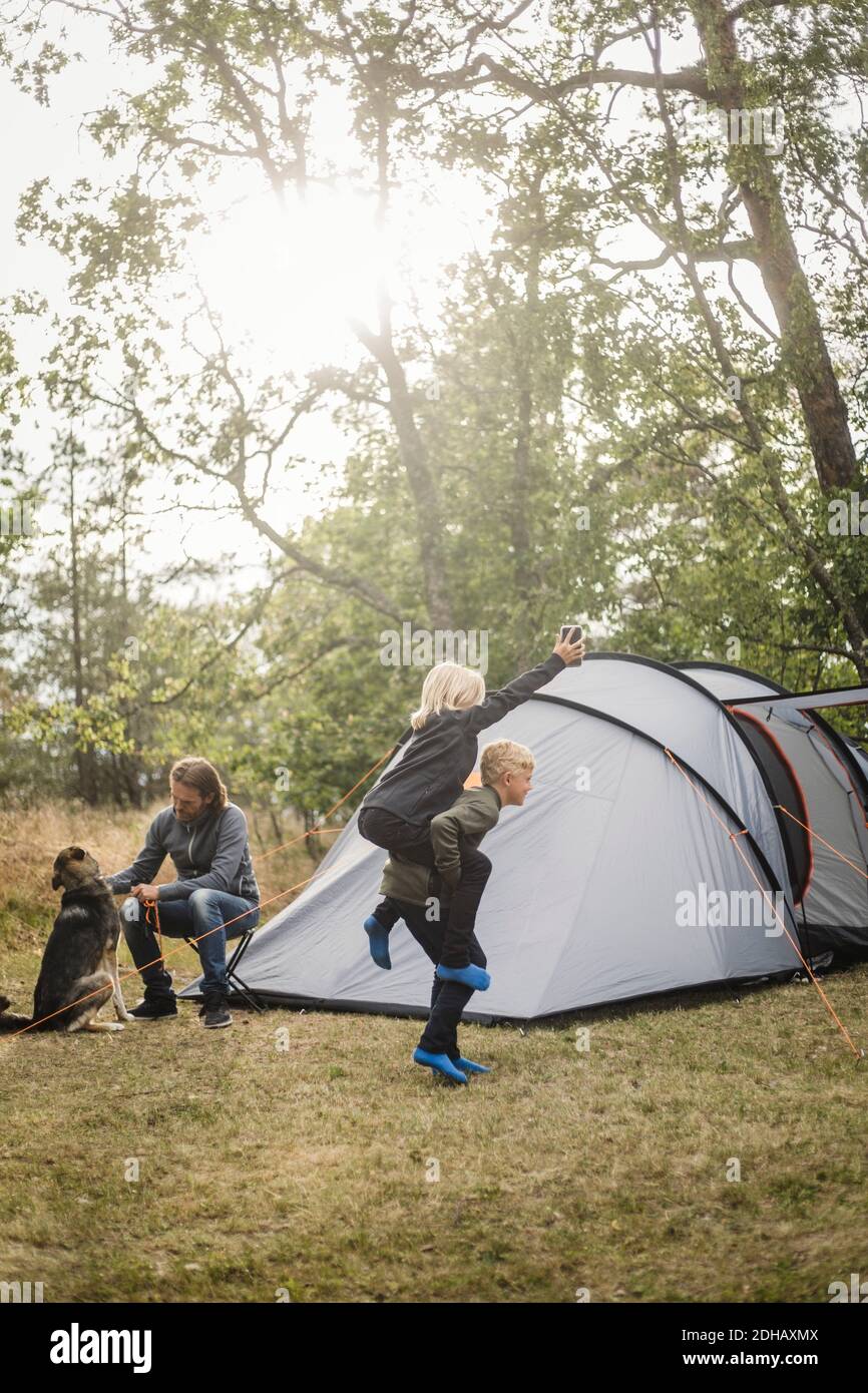 Homme assis par le chien pendant que les enfants jouent au camping-tente Banque D'Images