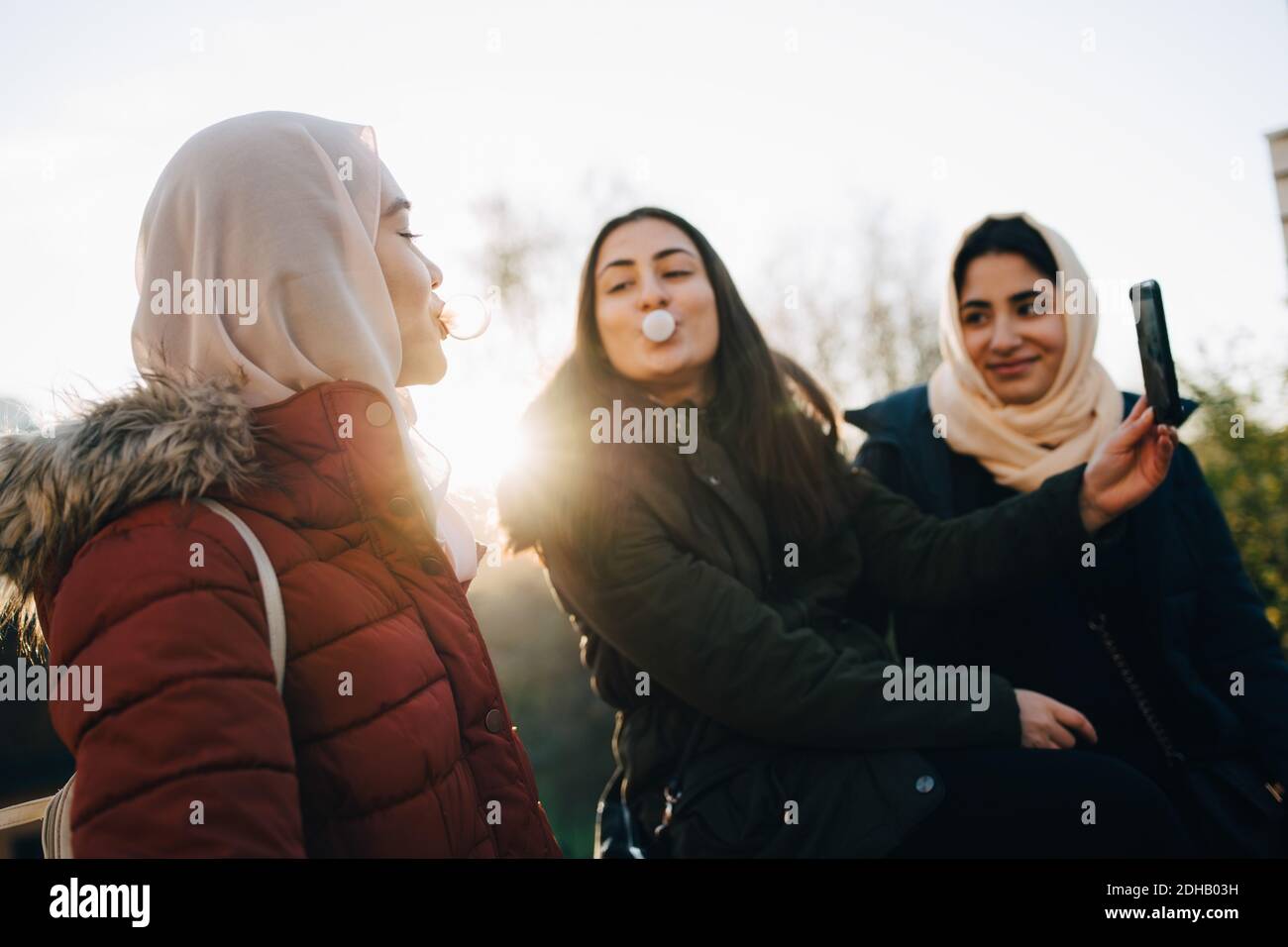 Des amies multi-ethniques soufflent des gommes à bulles tout en prenant le selfie contre ciel Banque D'Images