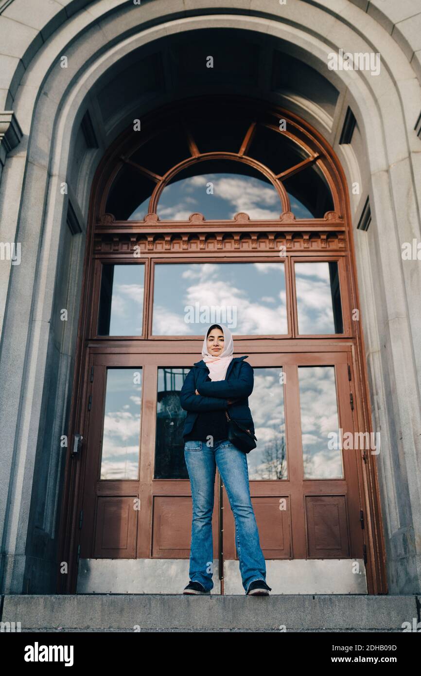 Portrait complet d'une jeune fille musulmane souriante debout avec les bras traversé à l'entrée de la ville Banque D'Images