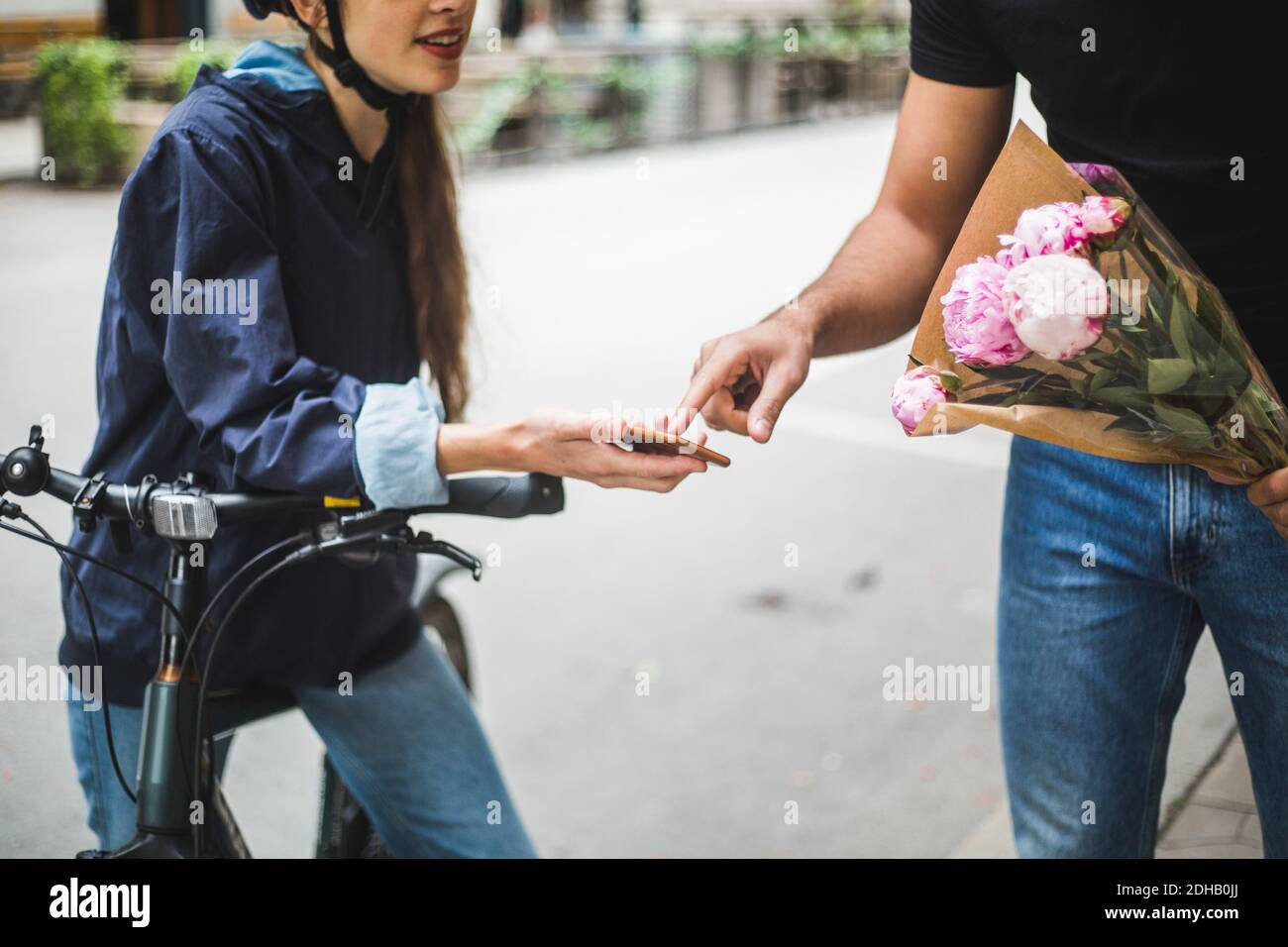 Section intermédiaire de la femme qui prend l'affiche du client lors de la livraison bouquet dans la rue en ville Banque D'Images