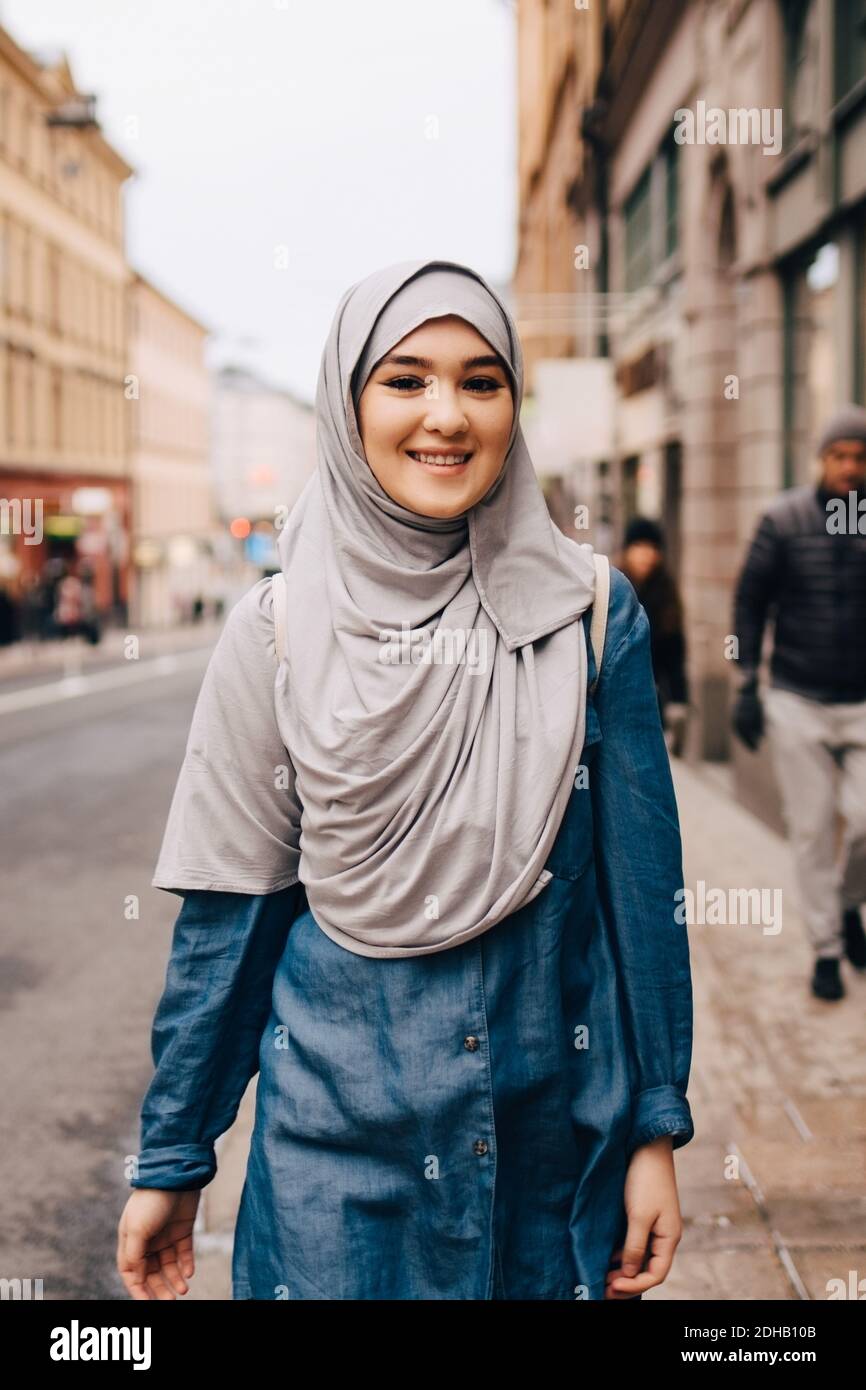 Portrait d'une jeune femme musulmane souriante portant le hijab marchant trottoir en ville Banque D'Images