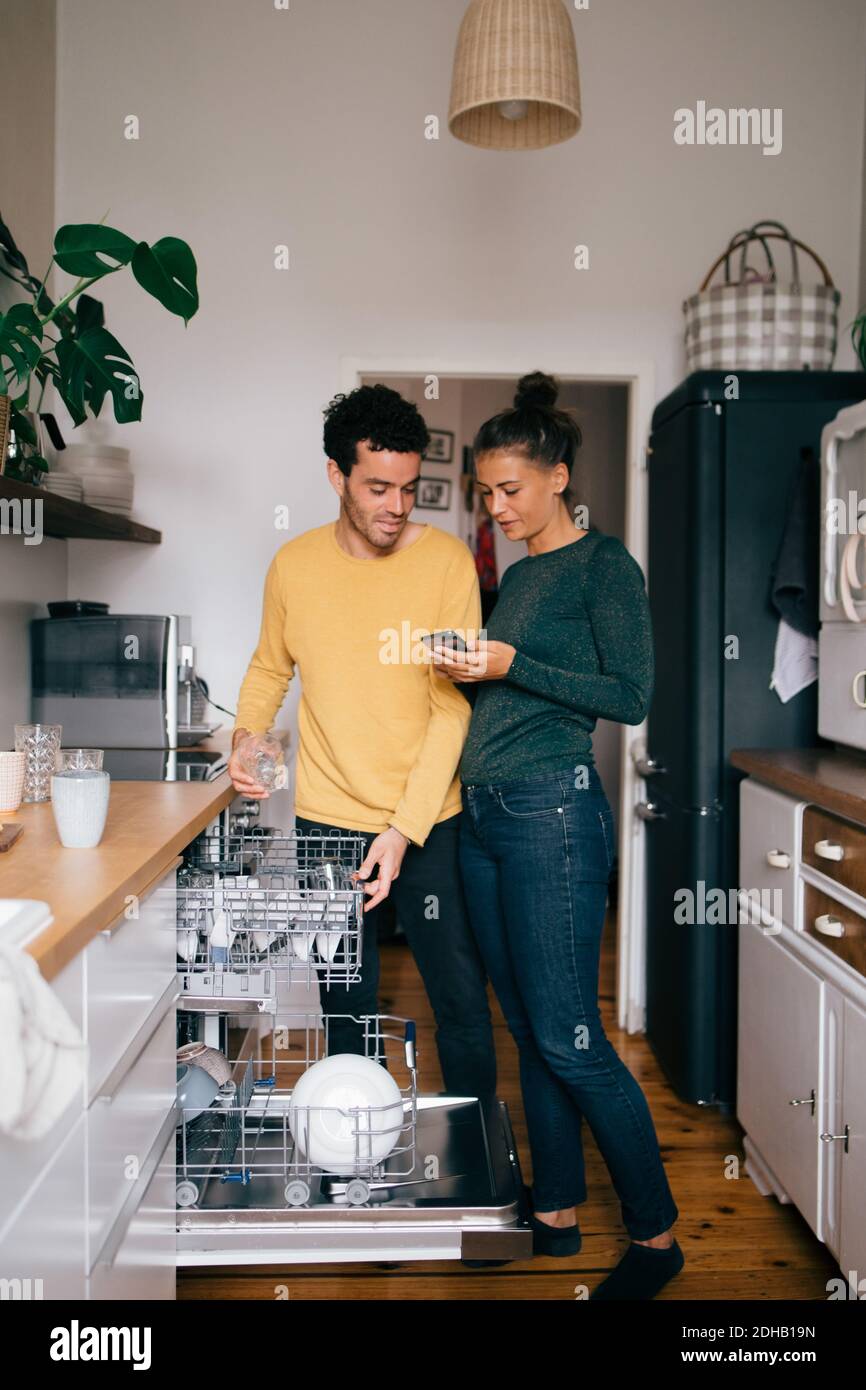 Femme montrant le téléphone portable à l'ami en étant debout dans la cuisine Banque D'Images