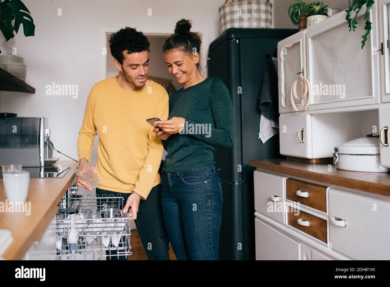 Femme souriant en montrant le smartphone à l'ami en étant debout dans la cuisine Banque D'Images