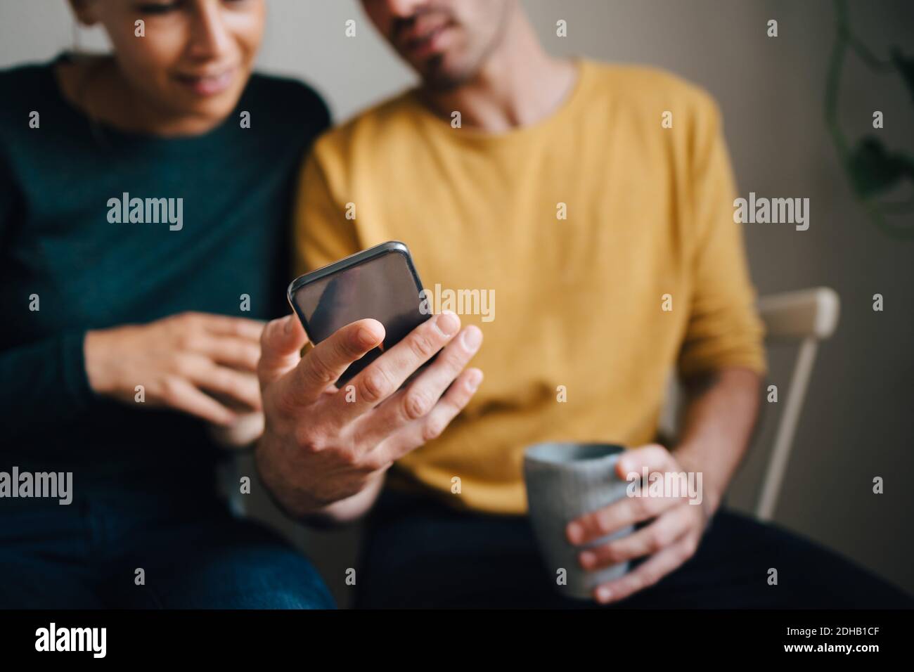 Mi-section de l'ami montrant le smartphone à la petite amie tout en ayant café à la maison Banque D'Images