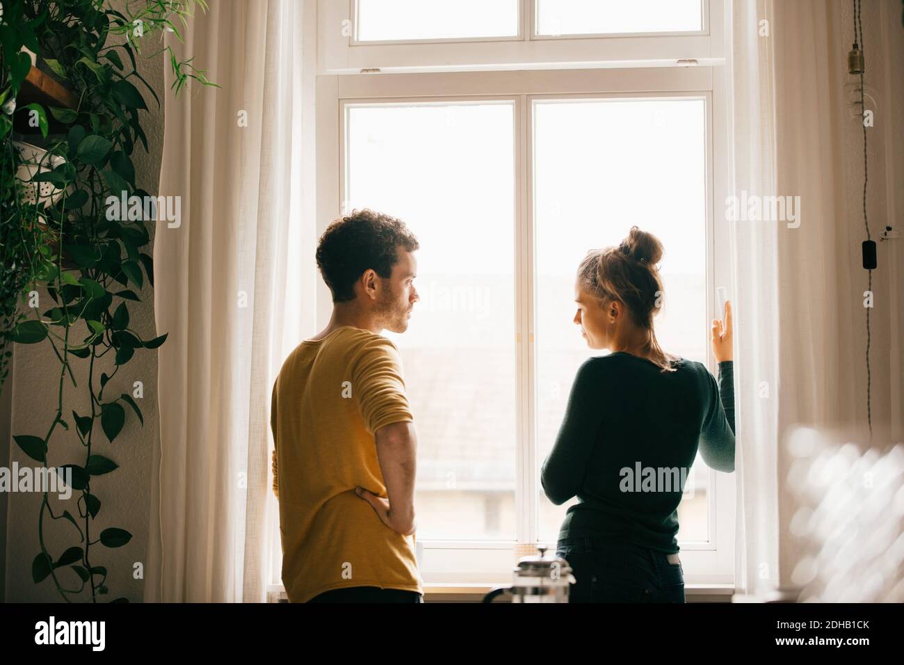 Couple parlant en se tenant près de la fenêtre à la maison Banque D'Images