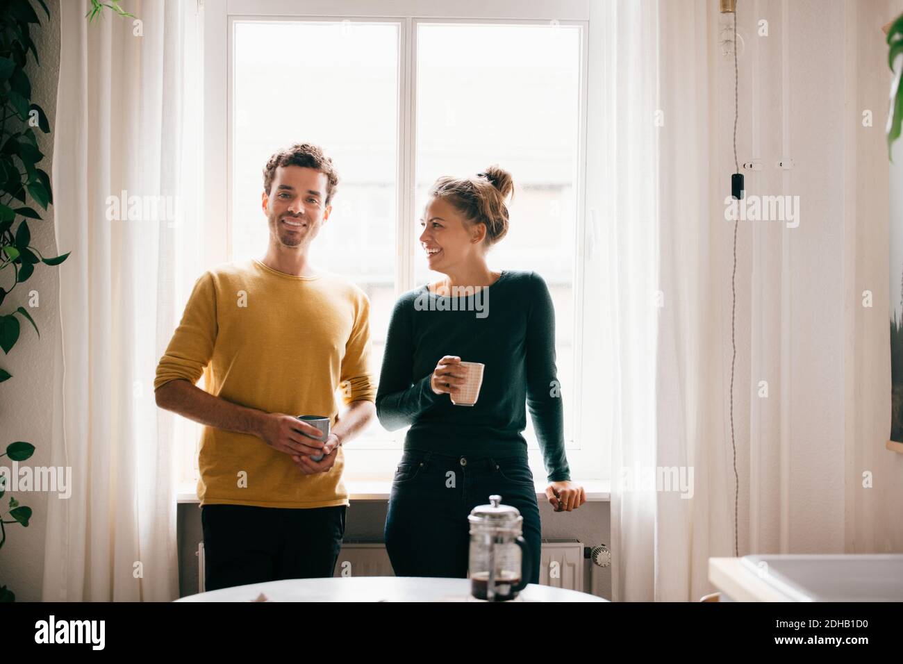 Couple heureux avec tasse de café contre fenêtre à la maison Banque D'Images